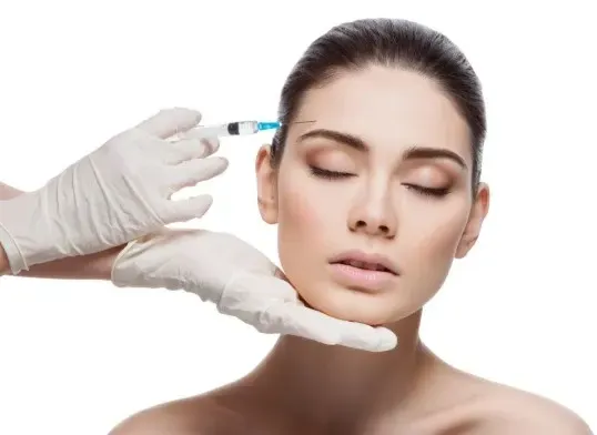 Gloved hands preparing a woman for a facial injection, with a syringe near her temple