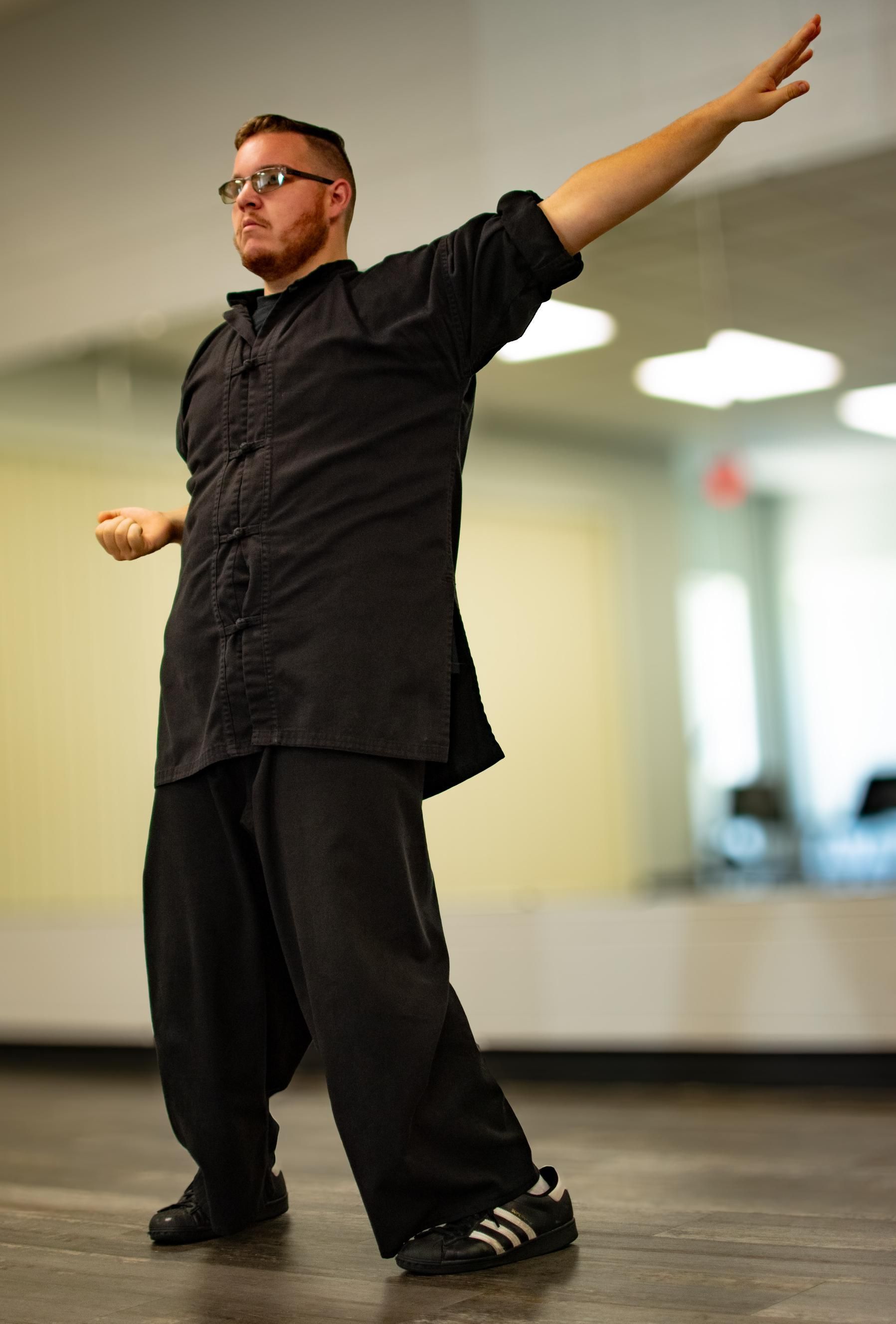 Man in black practicing martial arts, arm outstretched. Indoors, studio setting.