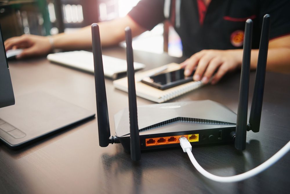 A Person Is Sitting At A Desk Using A Laptop And A Router — Lismore Computer Solutions In Lismore, NSW
