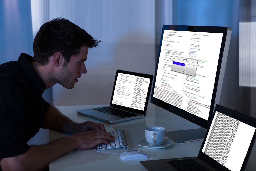A Man Is Typing On A Keyboard In Front Of Two Computer Monitors — Lismore Computer Solutions In Lismore, NSW