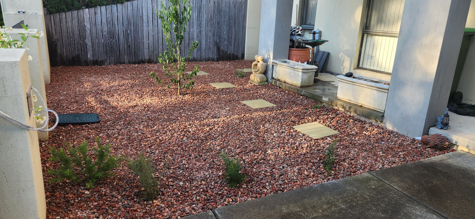 Small yard with red rock ground cover, stepping stones, small plants, and a wooden fence — Carro's Property Maintenance in Kaleen, ACT
