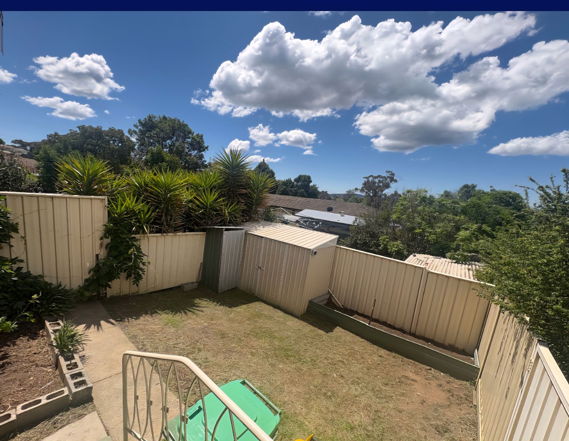 Backyard with white fences, patchy green grass, and blue sky with puffy white clouds  — Carro's Property Maintenance in Weston Creek, ACT