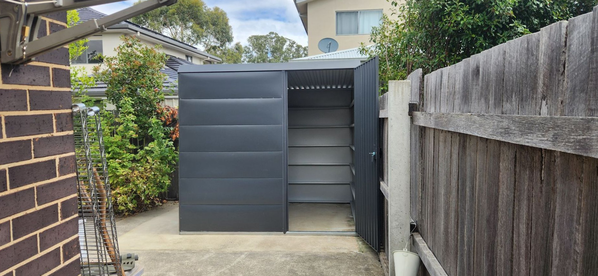 Black shed with sliding door and open door on a concrete patio, beside a wooden fence — Carro's Property Maintenance in Kaleen, ACT