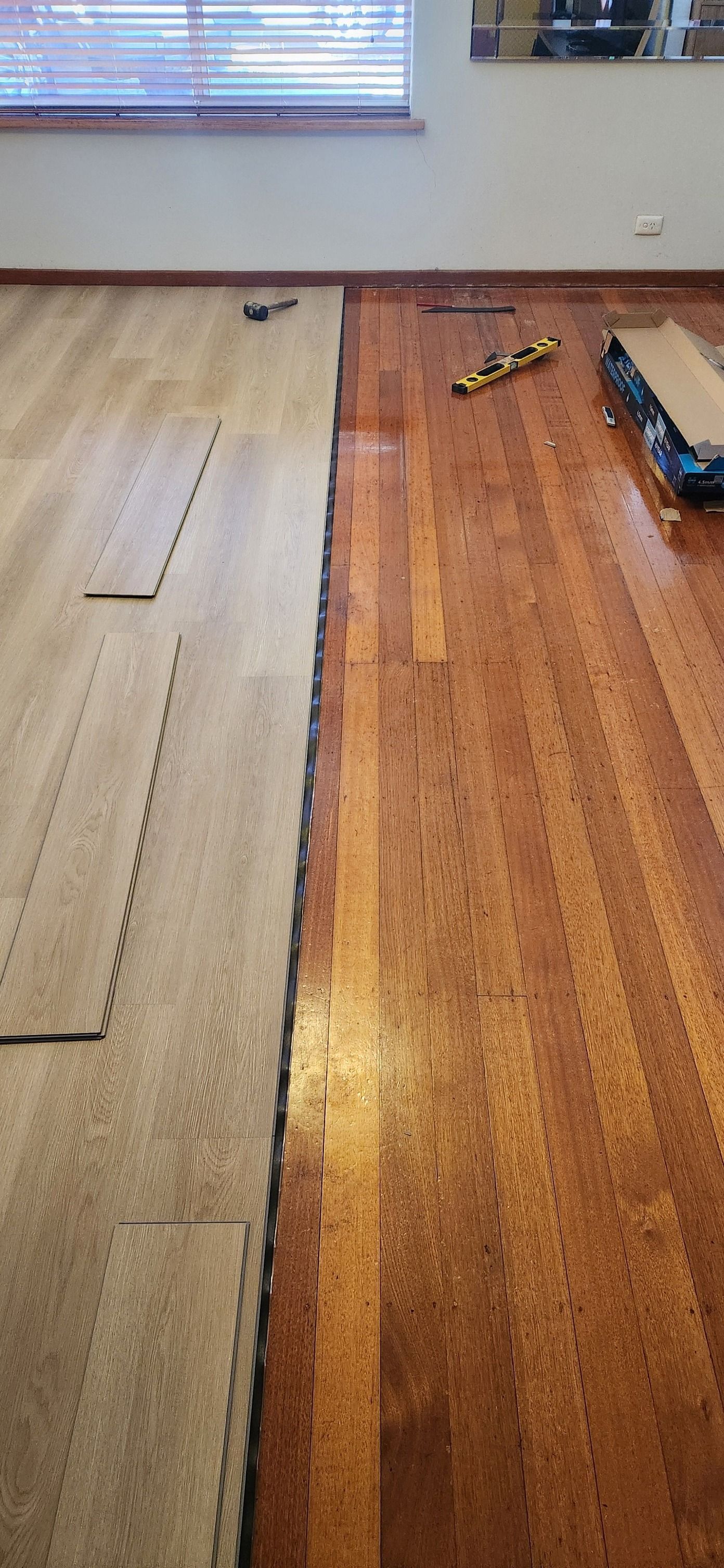Floor installation in progress; wood flooring next to lighter-coloured flooring. Tools and window in the background  — Carro's Property Maintenance in Kaleen, ACT