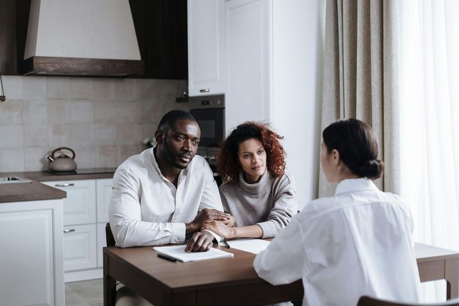 A man and woman are sitting at a table talking to a woman.