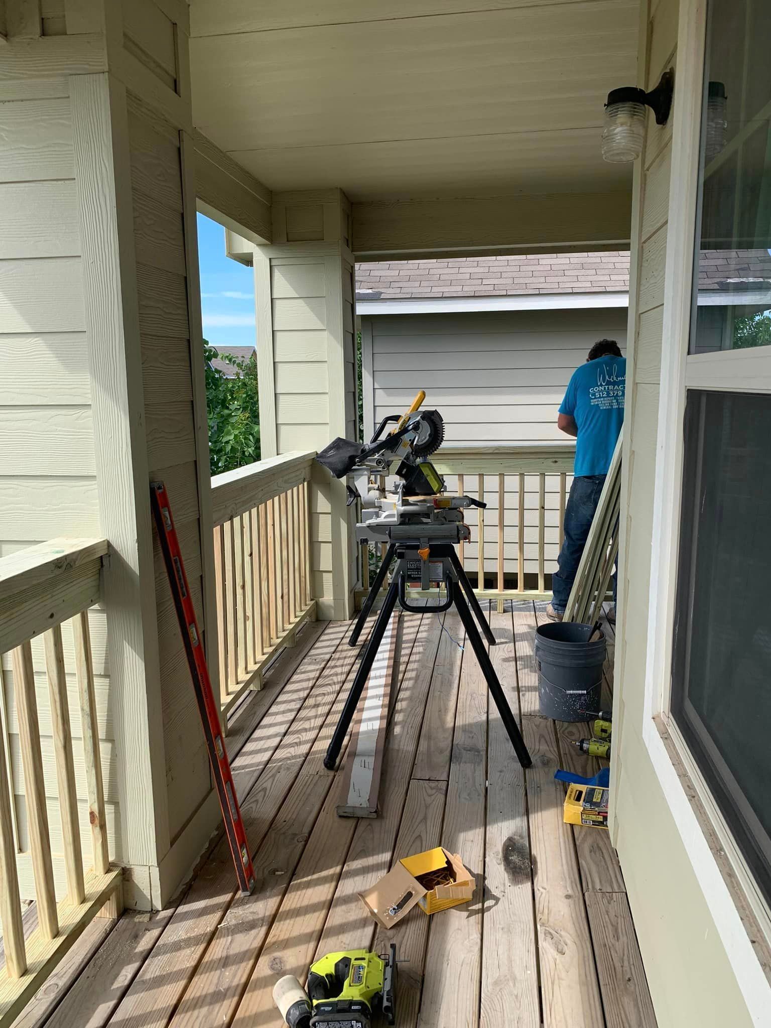 A man is standing on a porch using a circular saw.