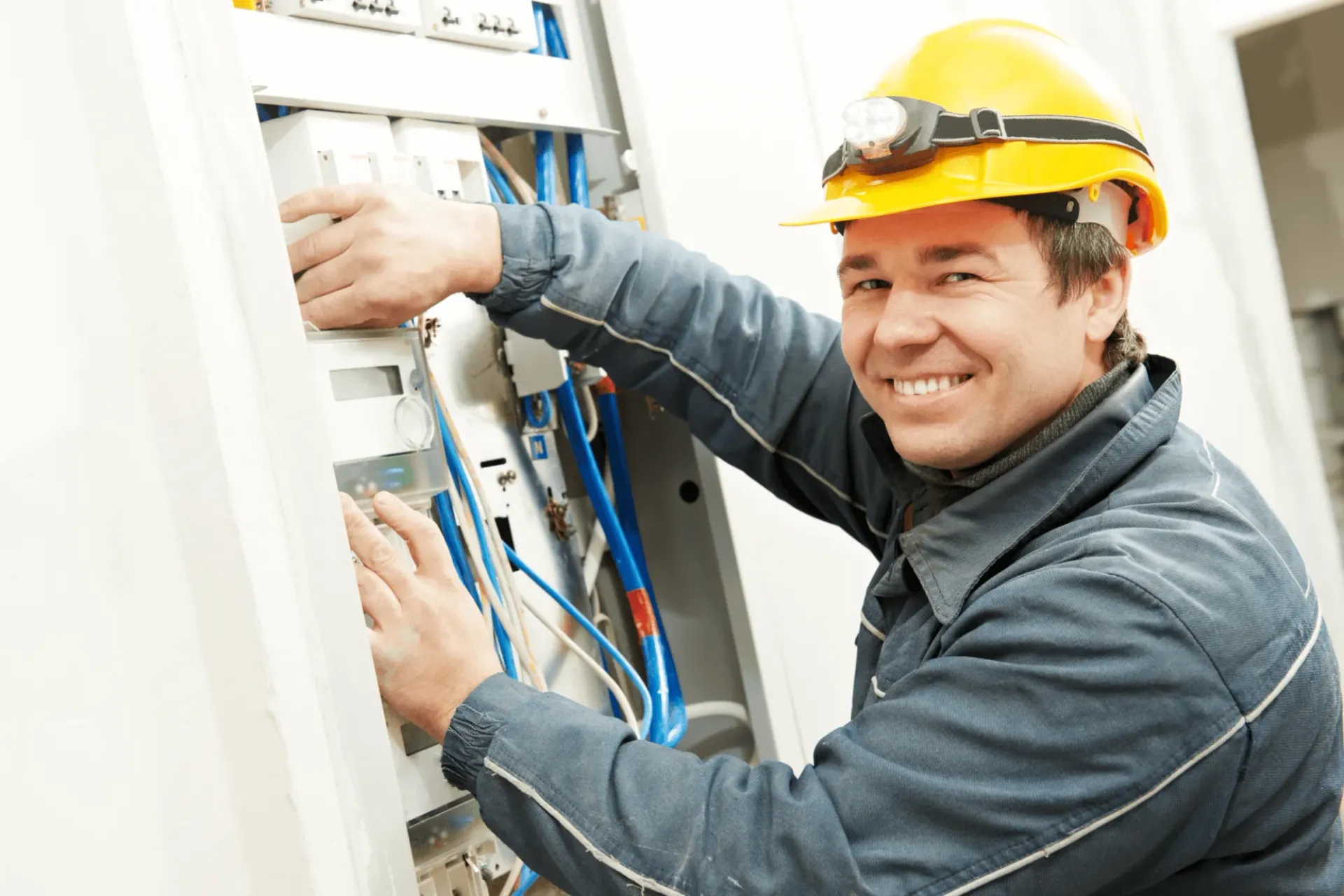 A man wearing a hard hat is working on an electrical box.