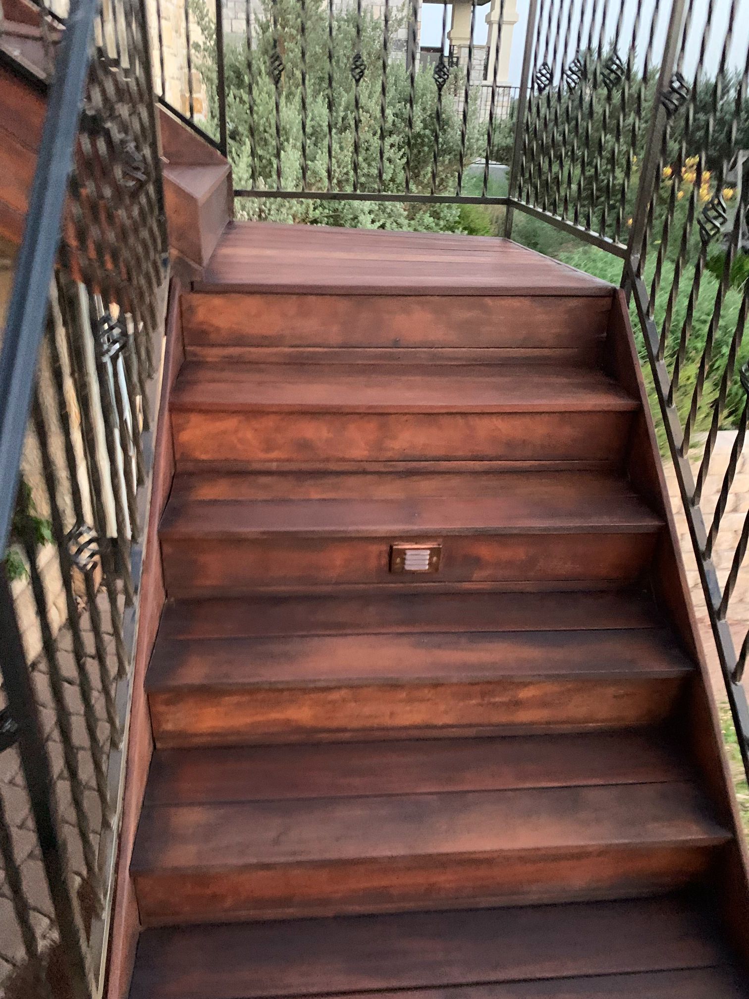 A set of wooden stairs with a metal railing leading up to a balcony.