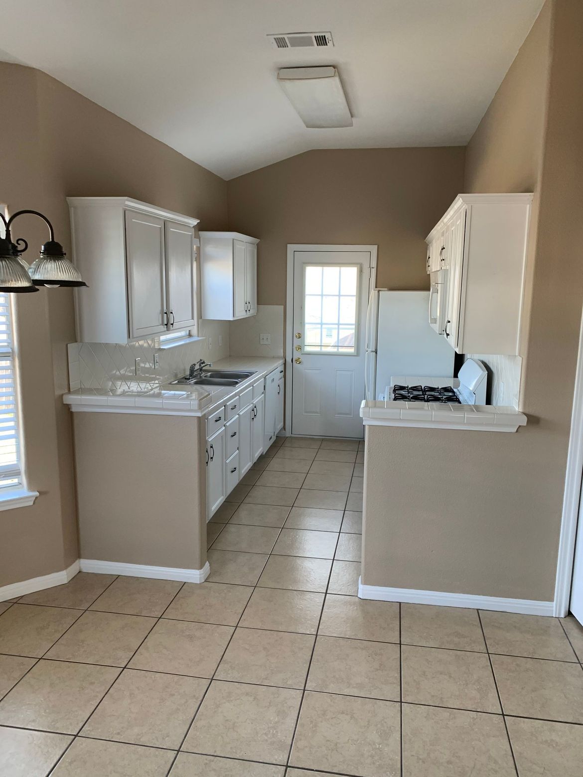 A kitchen with white cabinets , a stove , a refrigerator and a window.
