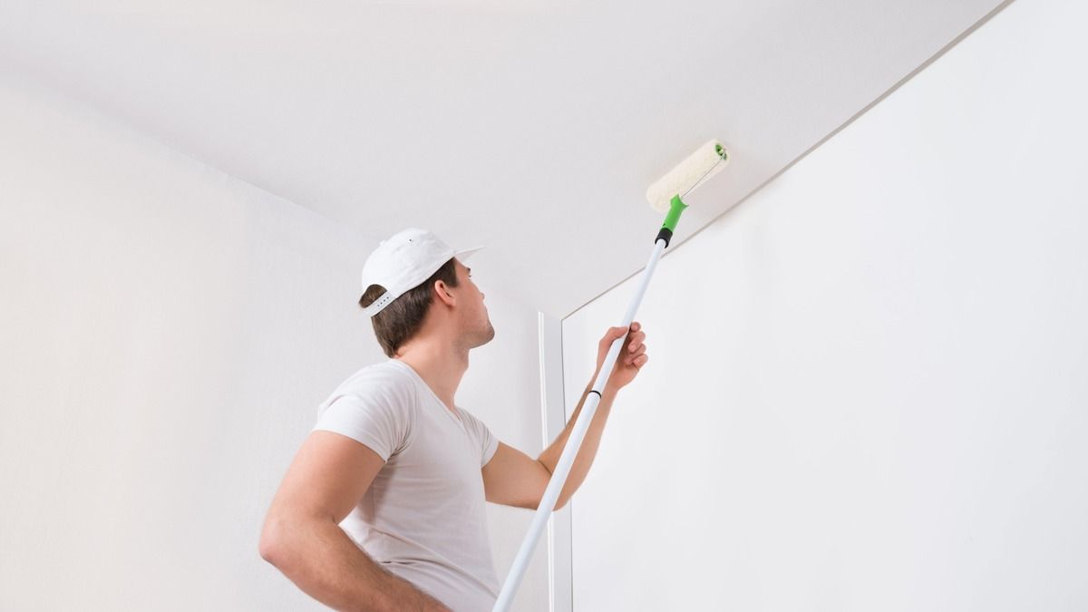 A man is painting the ceiling with a paint roller.