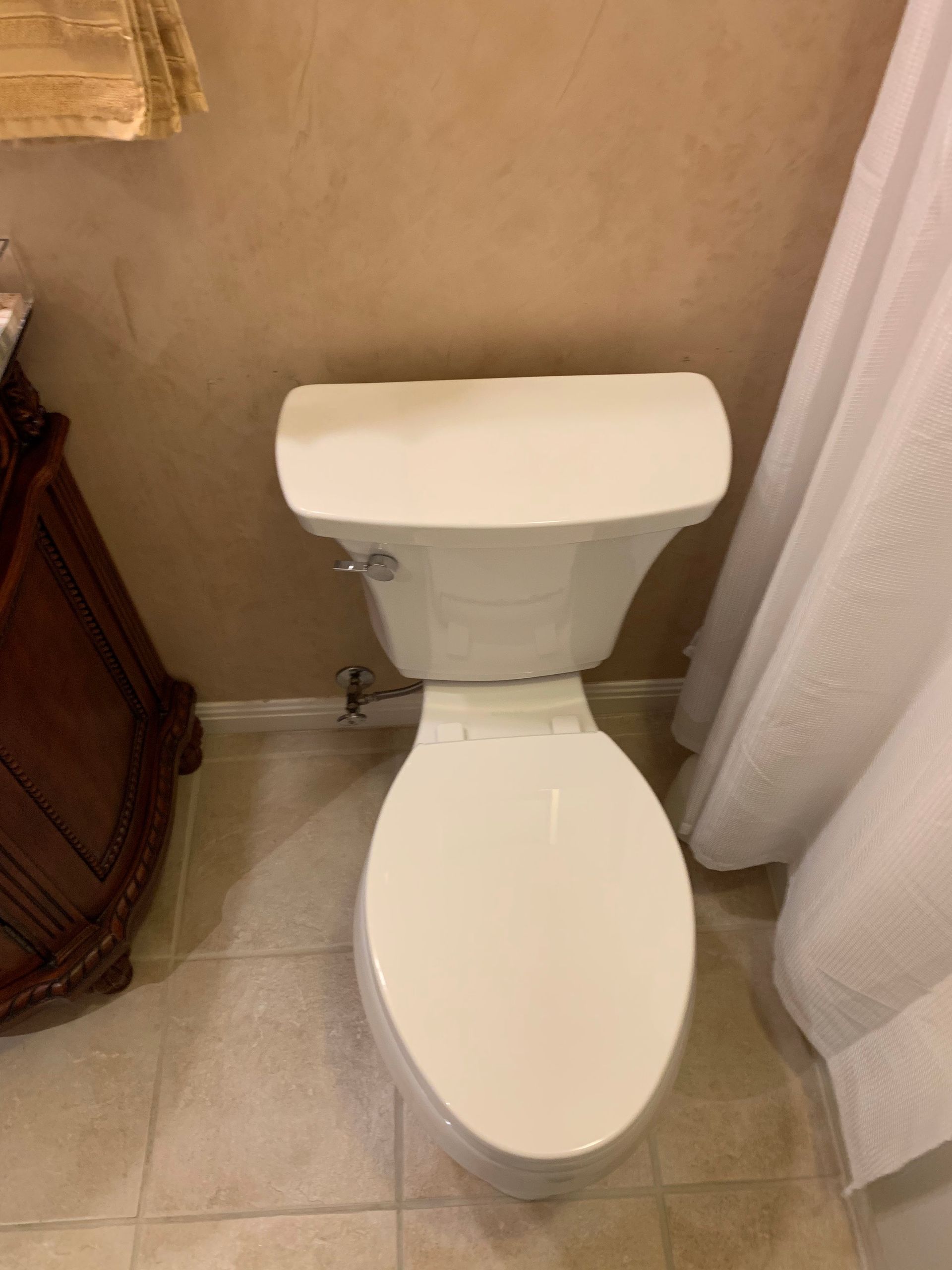 A white toilet is sitting in a bathroom next to a shower curtain.