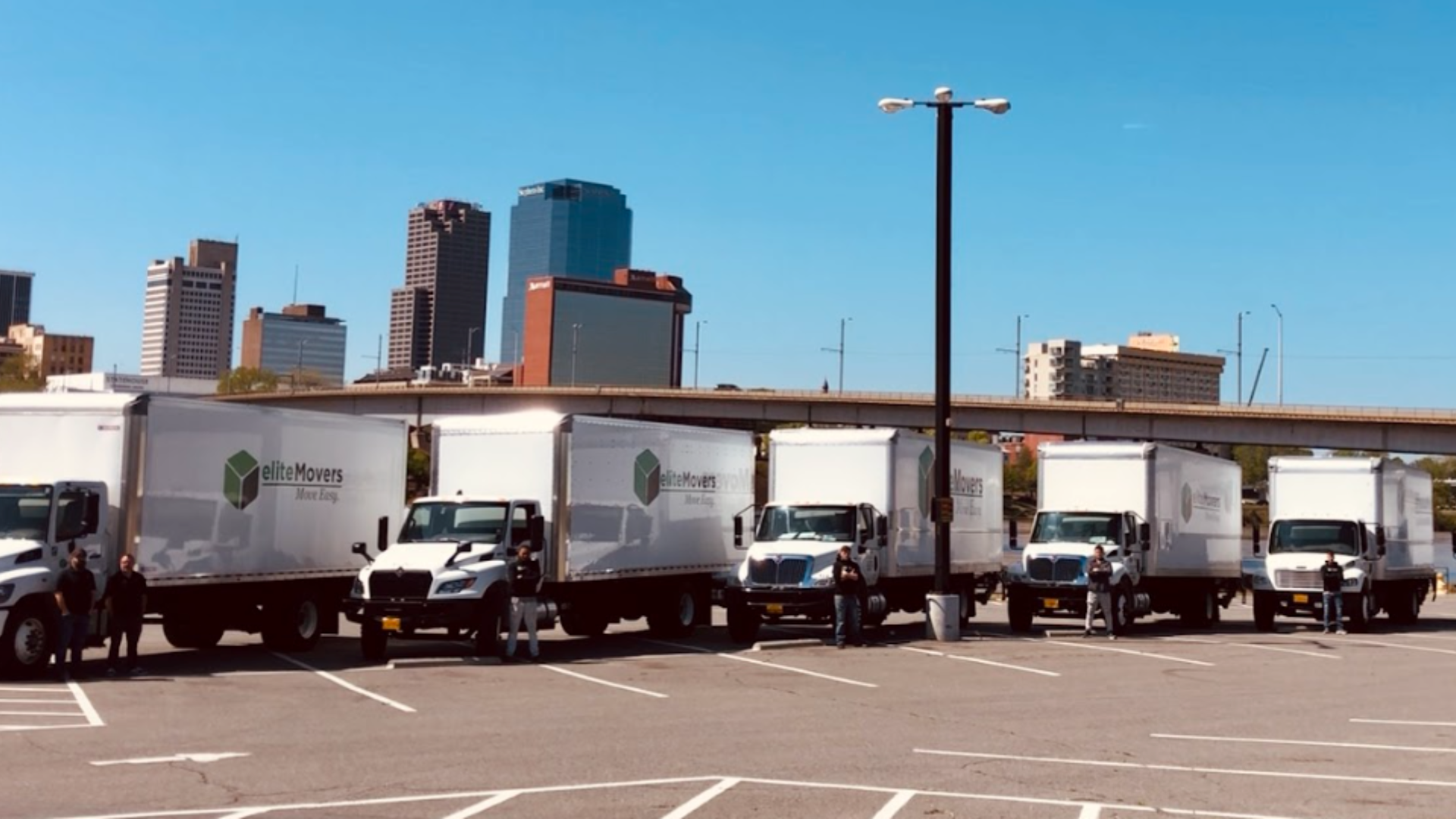Several white delivery trucks parked in a lot with a city skyline in the background