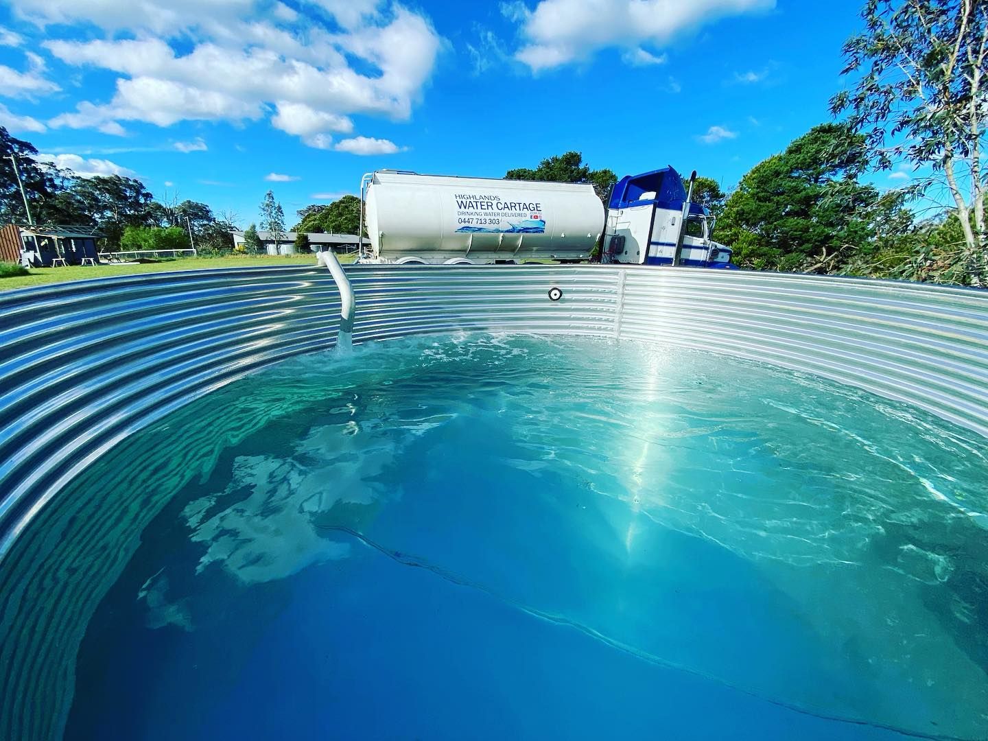 Water tank filling a corrugated metal stock tank on a sunny day — Highlands Water Cartage in South West Sydney, NSW