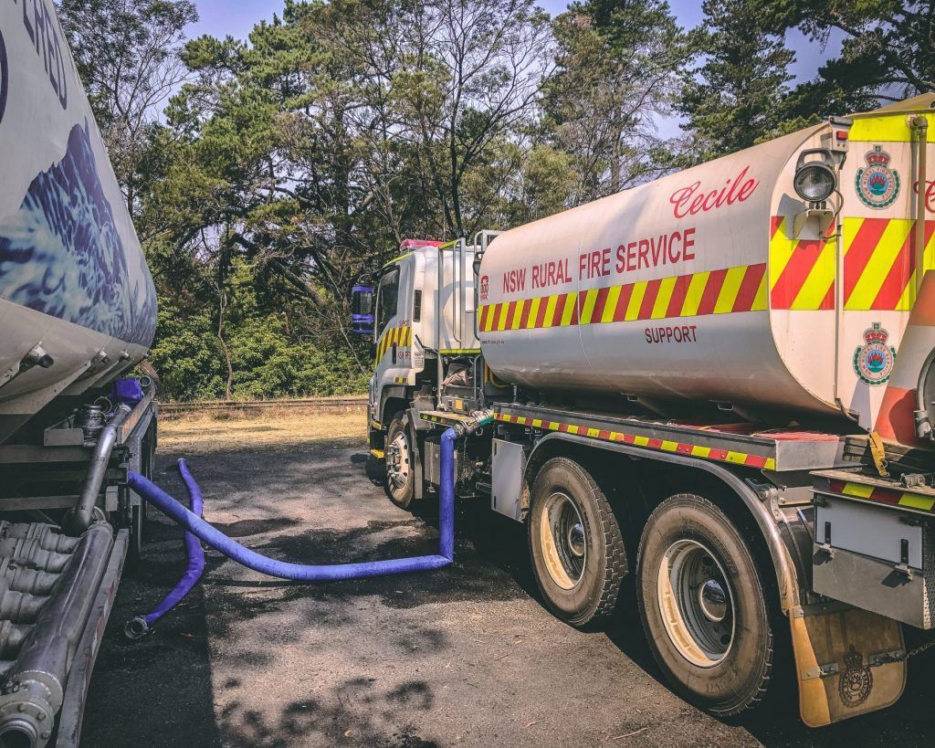 Fire truck being refueled; blue hoses connecting the tanks. Trees in background — Highlands Water Cartage in Glenquarry, NSW