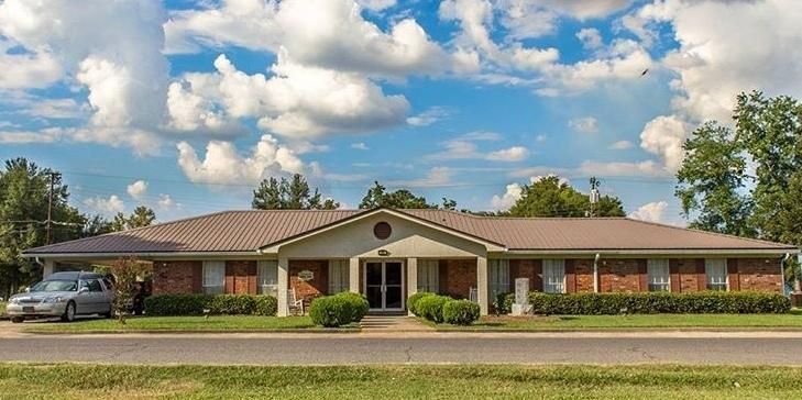 Single-story tan house with a carport, front lawn, and cloudy blue sky