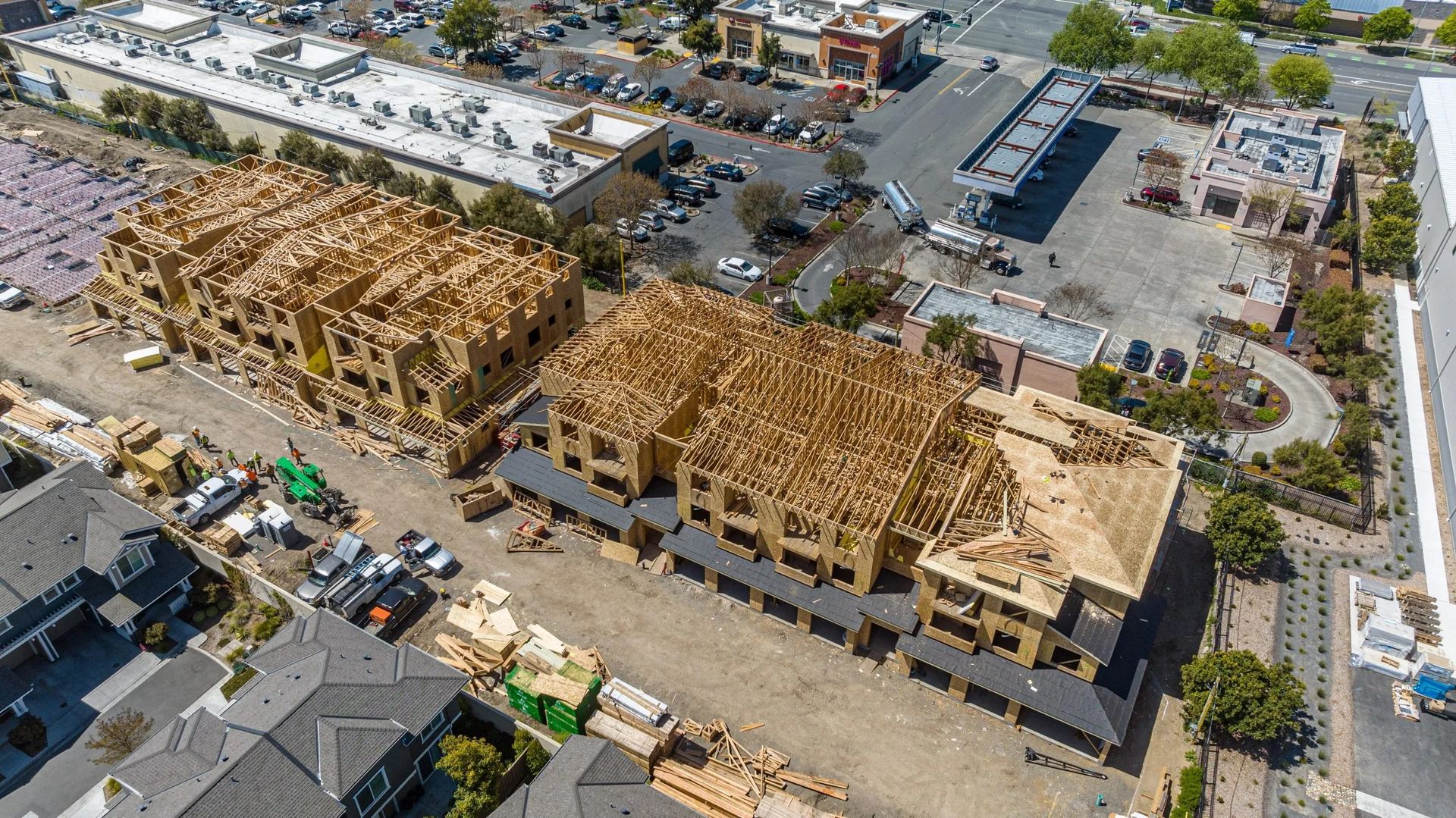 Aerial view of two large wooden building frames under construction beside a parking lot and road.