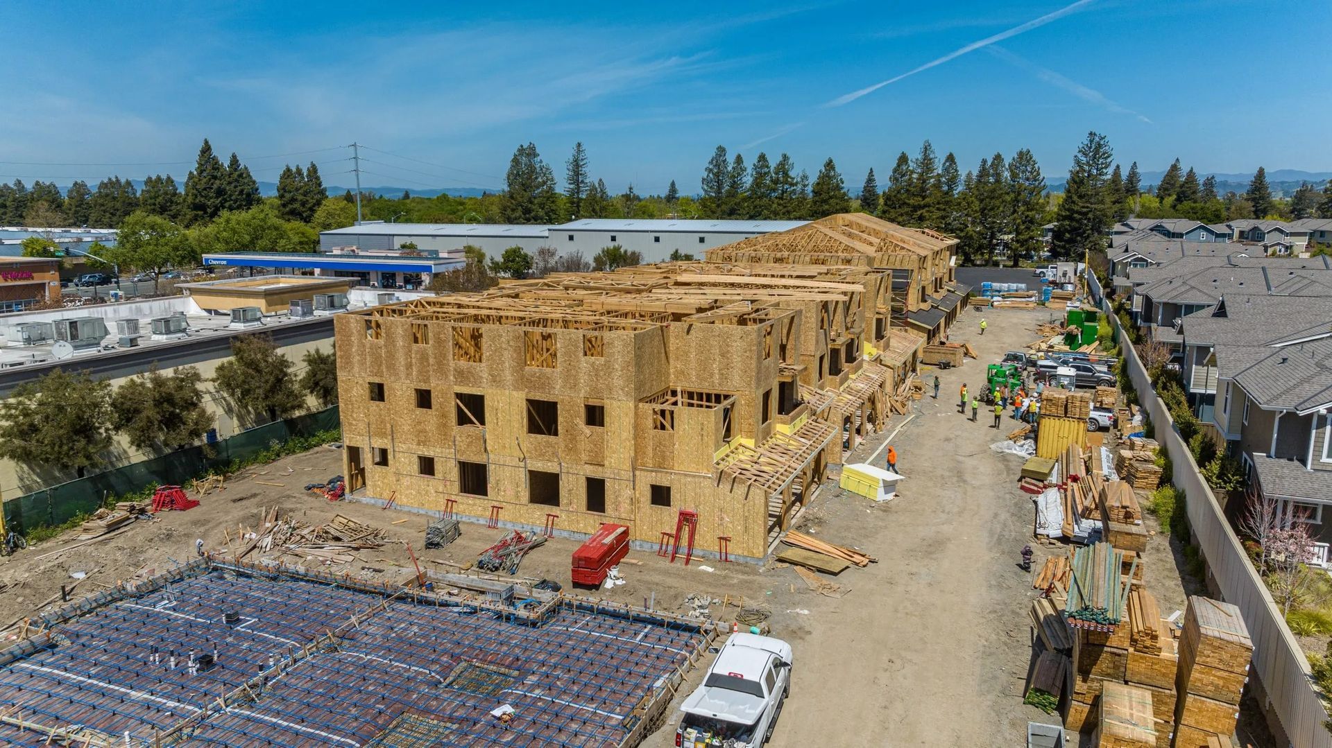 An aerial view of a multi-story wooden apartment building under construction near a prepared foundation.