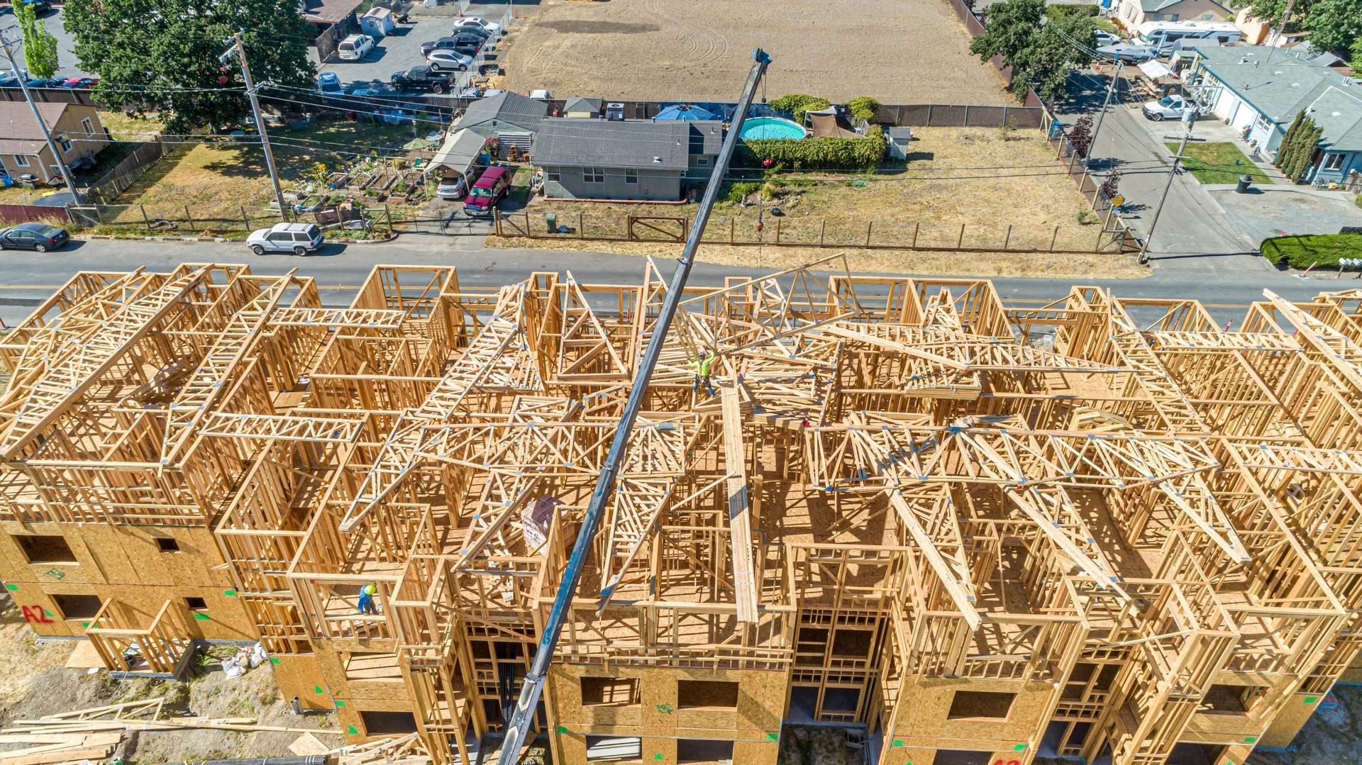 Aerial view of a multi-story wooden apartment building under construction, with framing exposed and a crane arm visible.