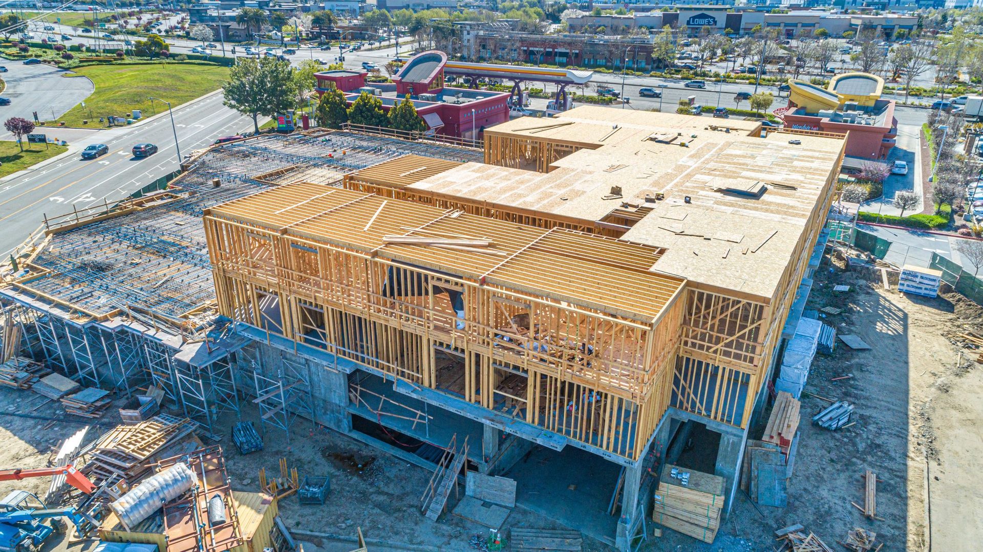 An aerial view of a multi-story building under construction with exposed wooden framing and a plywood roof deck.