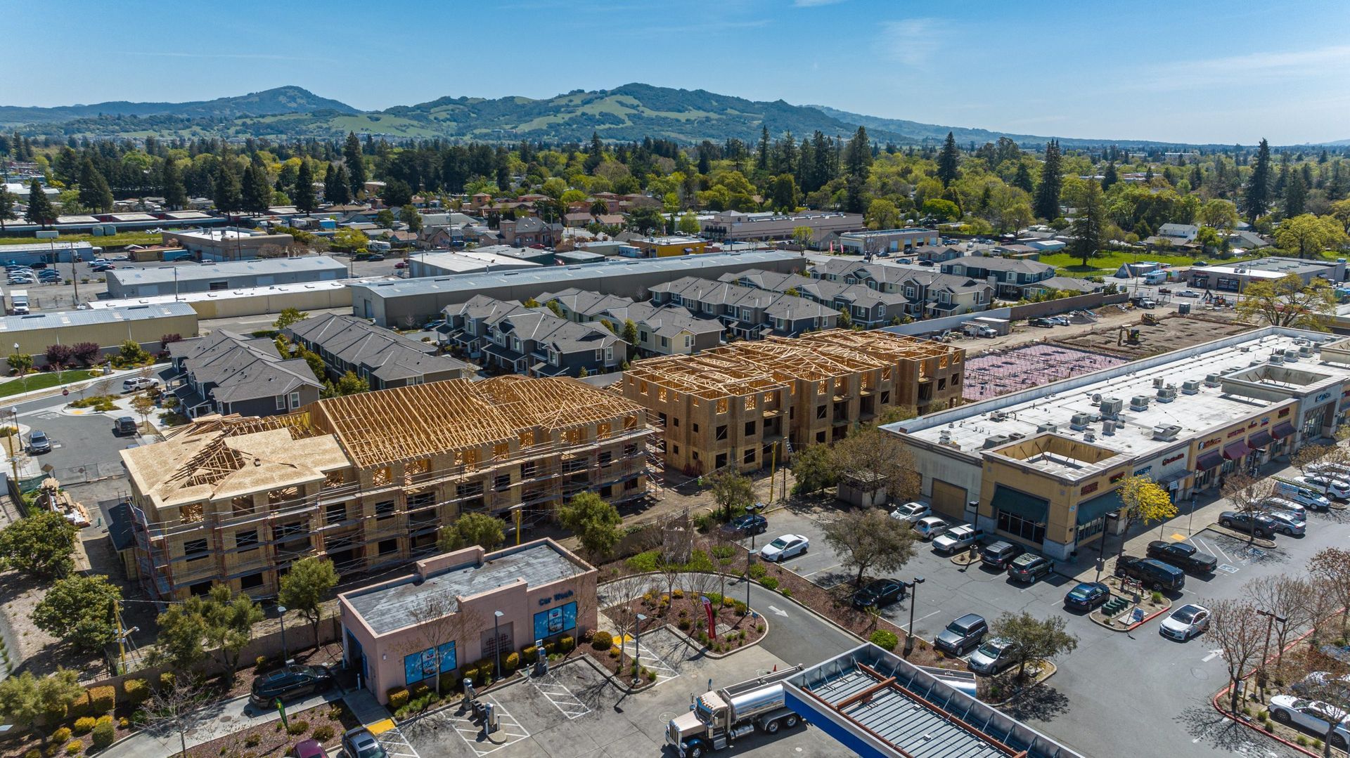 Aerial view of a partially constructed multi-story apartment building frame in a suburban setting with a parking lot.