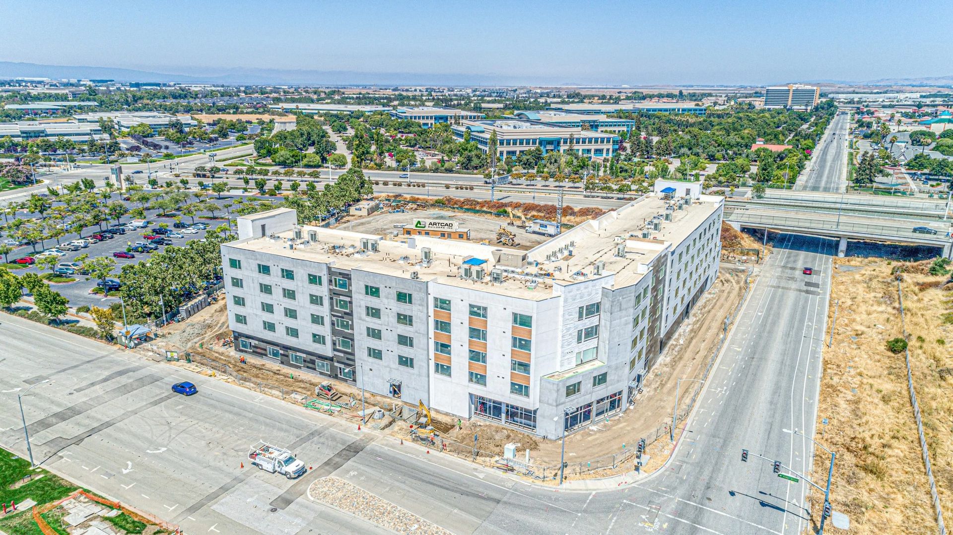Aerial view of a white apartment building under construction beside a road in a suburban area.