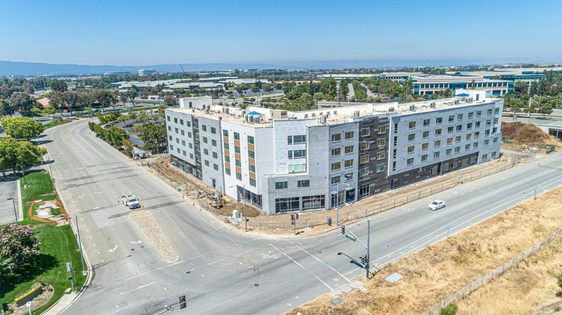 Aerial view of a white apartment building at a road intersection in a suburban area.