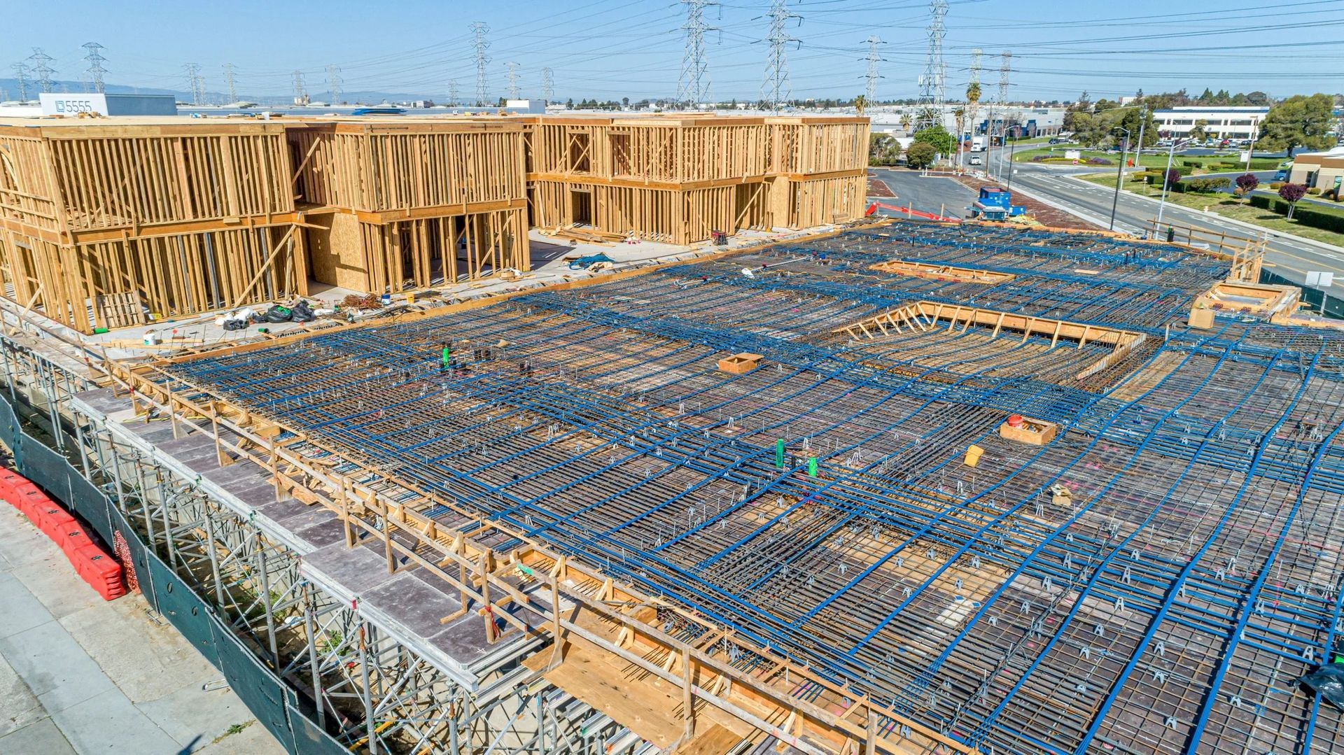 An aerial view of a construction site showing wood-framed wall structures next to a concrete foundation with rebar grids.