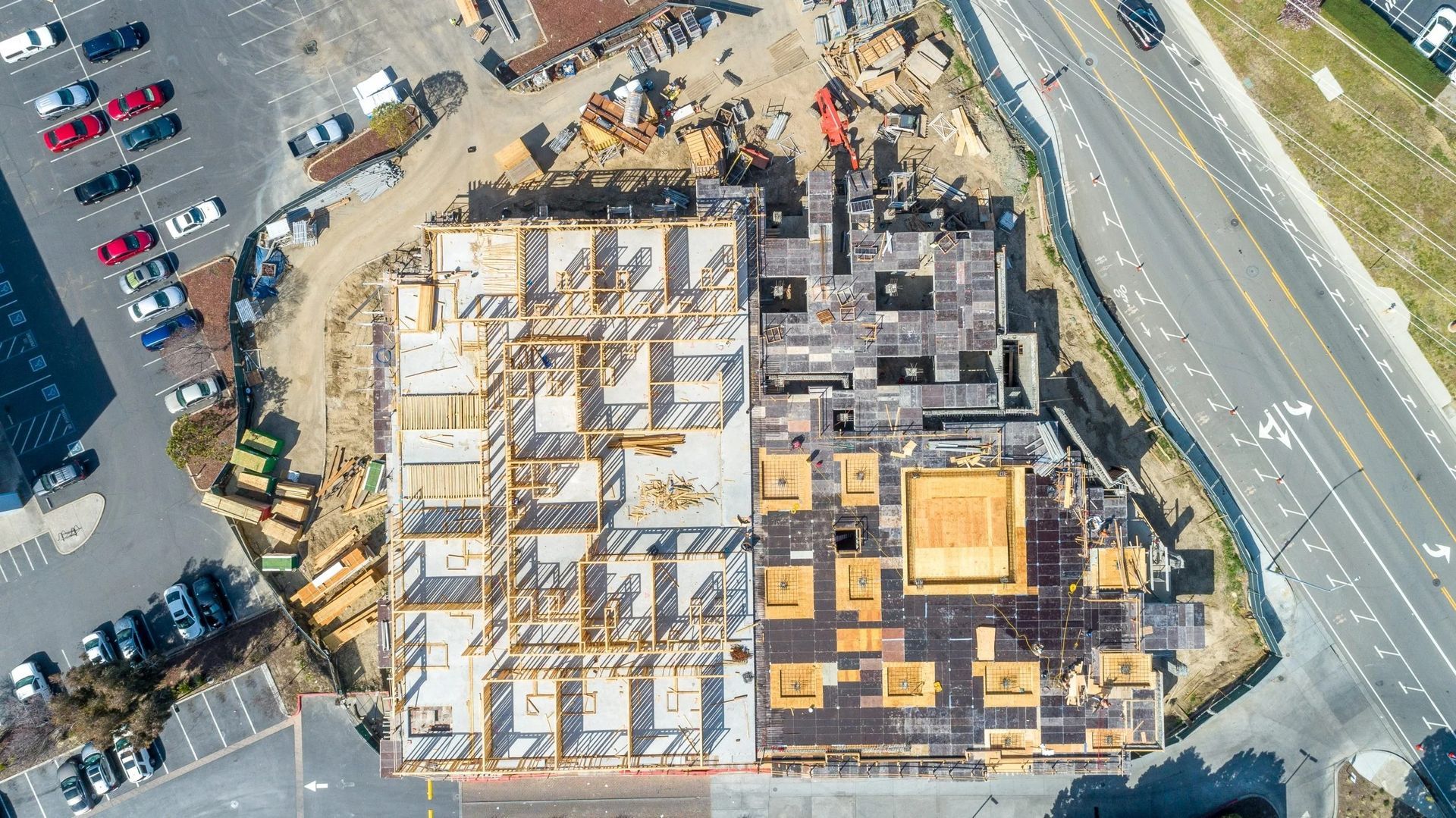 Aerial view of a building under construction, showing a wooden frame on the left and a partially covered roof on the right.