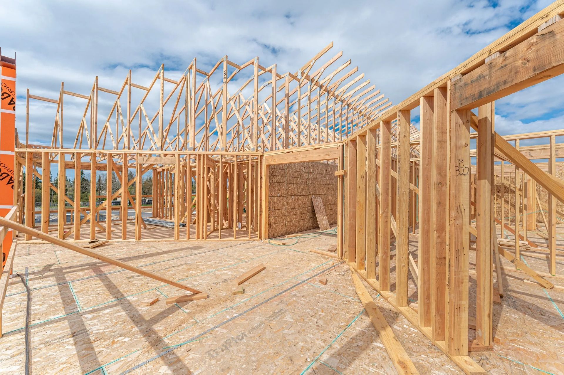 Wood-framed house under construction on a sunny day, with exposed roof trusses and exterior walls