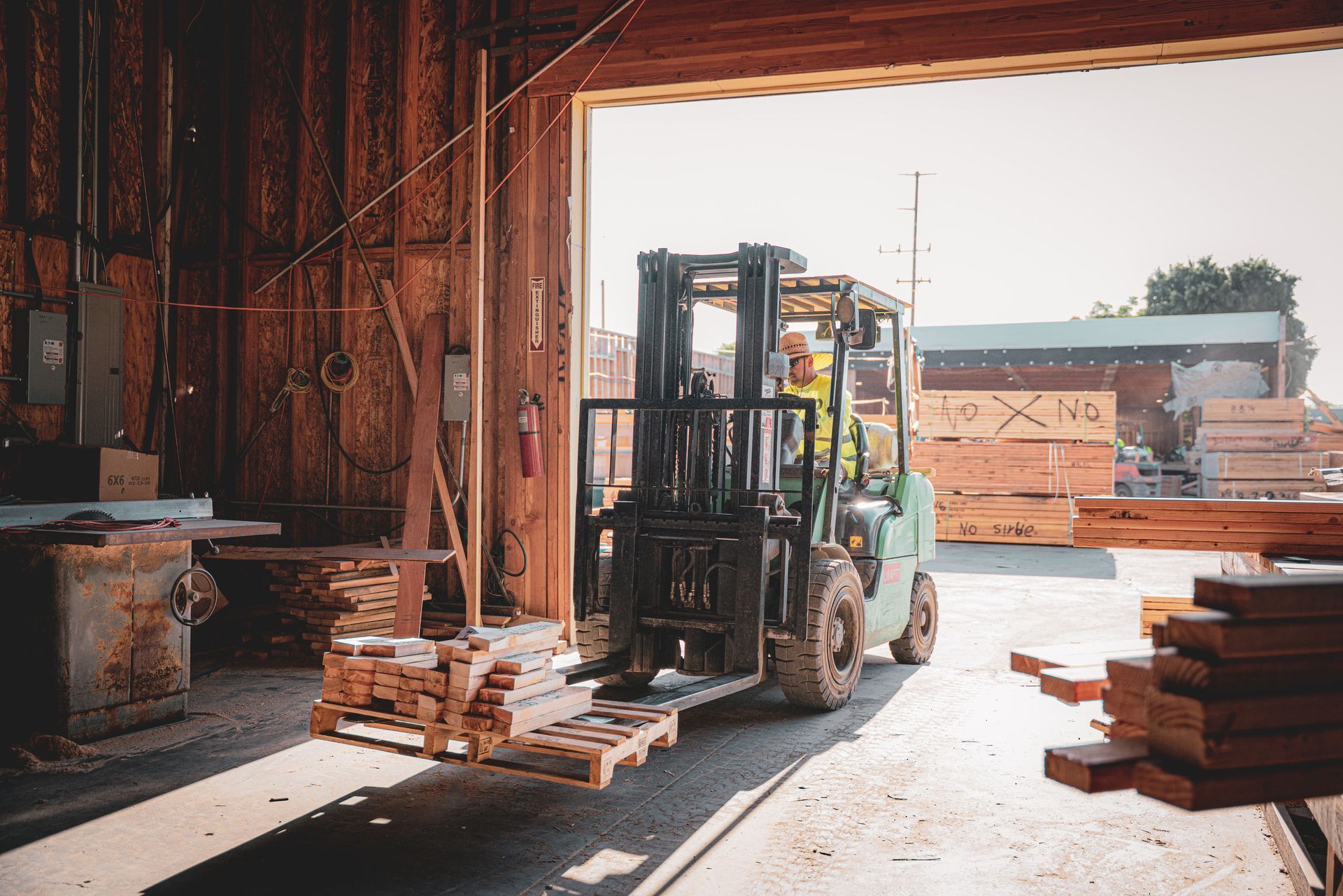 Forklift carrying lumber inside a warehouse with stacks of wood by the open loading bay