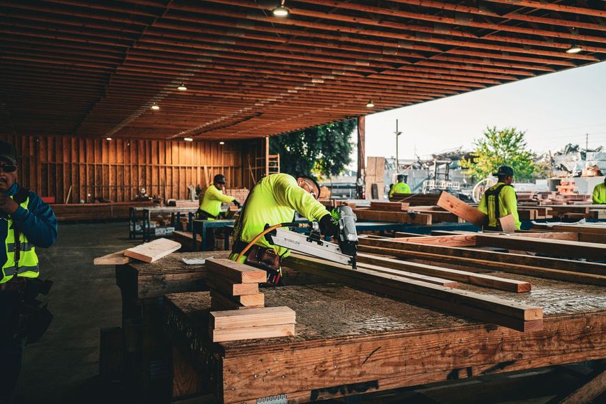 Construction workers in neon vests assembling wooden beams under a covered outdoor structure