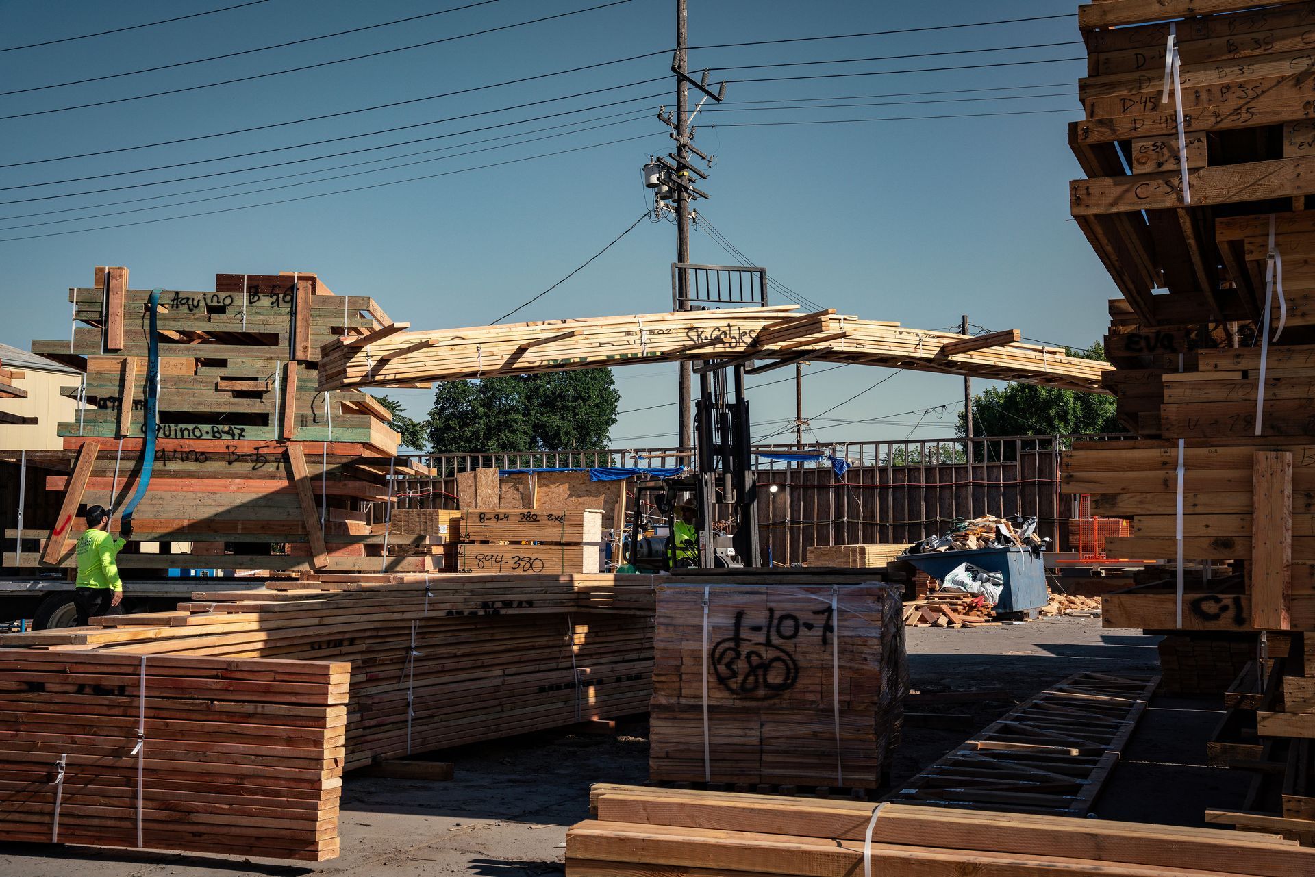Workers operating machinery in a wood shop with stacked lumber in the foreground