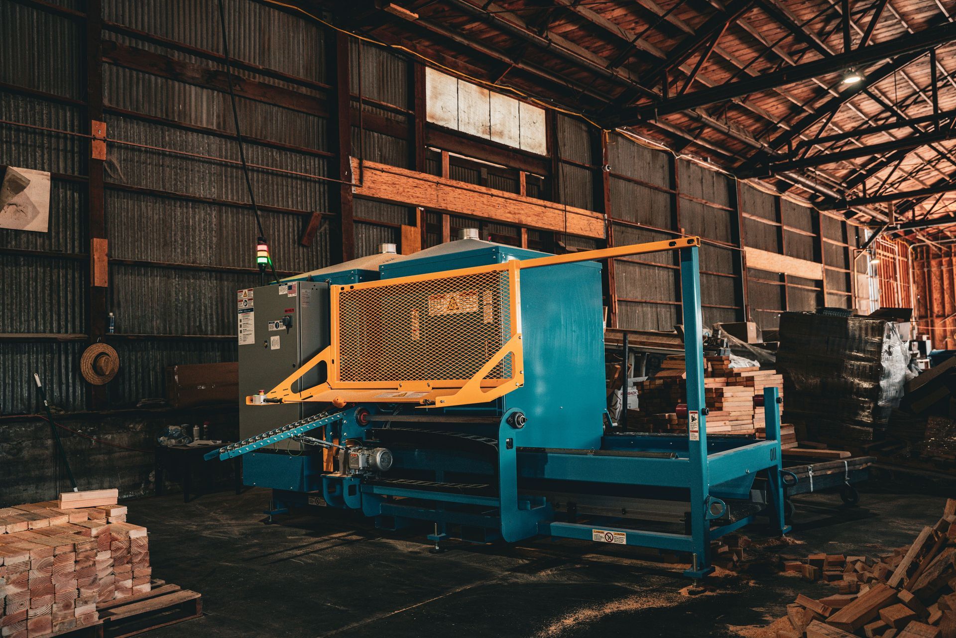 Industrial machine in a warehouse, with yellow and blue metal framework among stacks of materials.