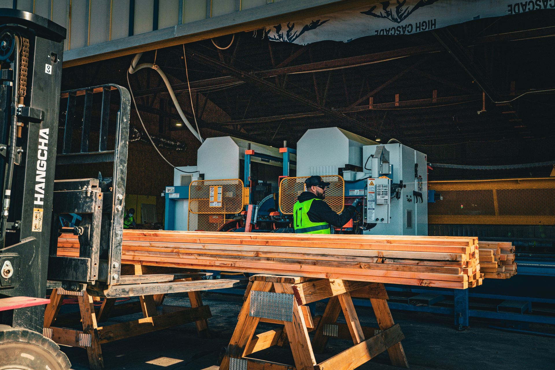 Workers operating machinery in a wood shop with stacked lumber in the foreground