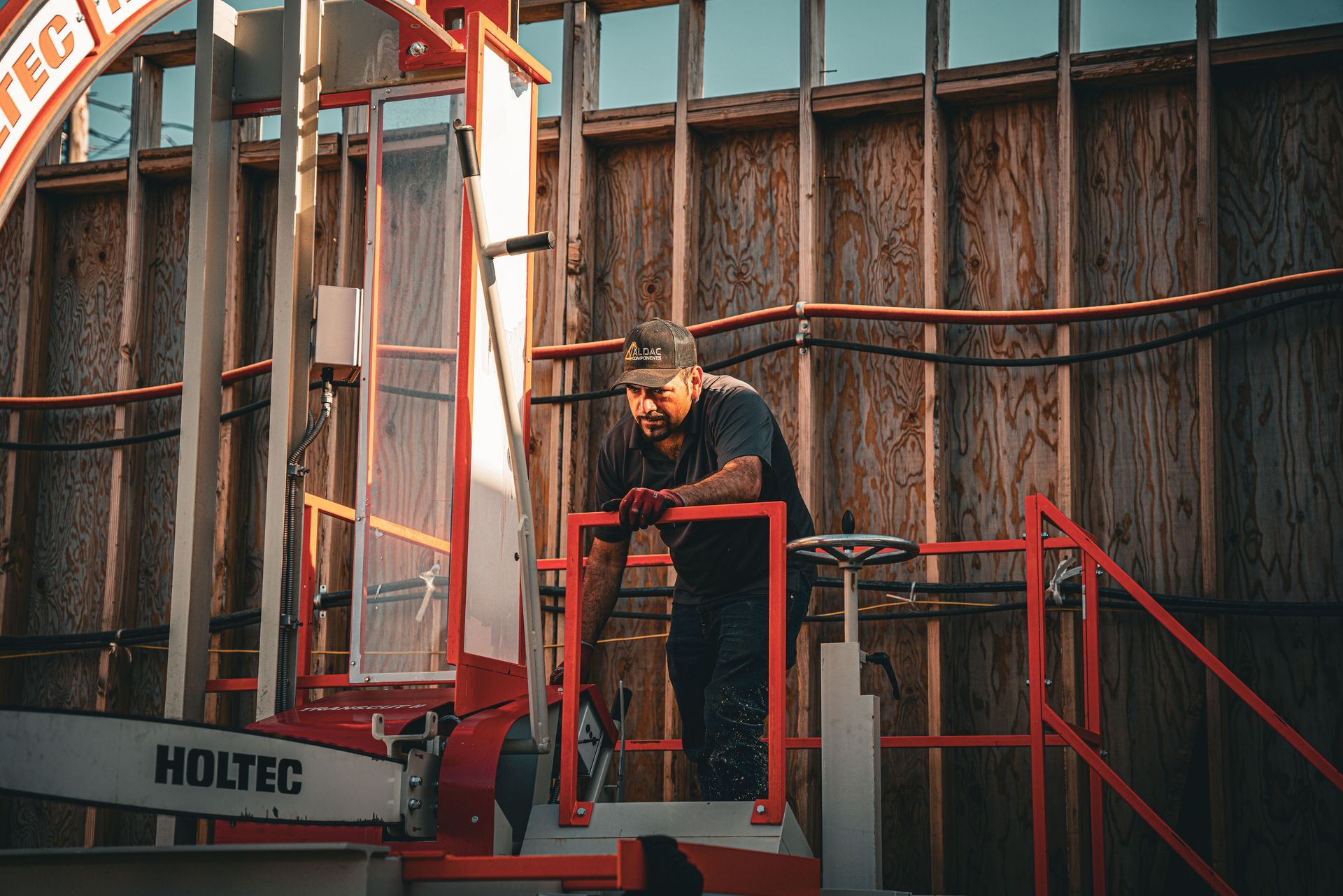 Worker operating a red lift platform beside a building under construction