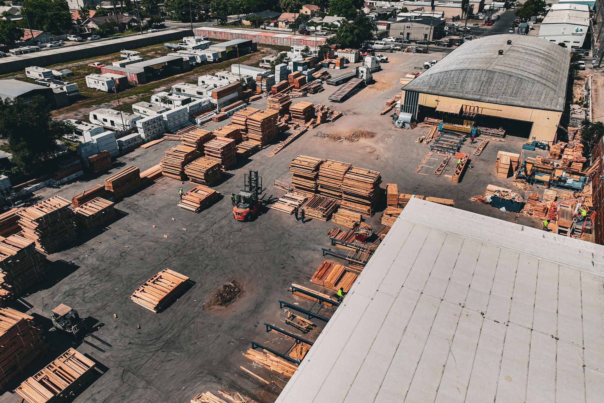 An aerial view of a multi-story hotel under construction, next to a highway and a large parking lot, under a clear sky.