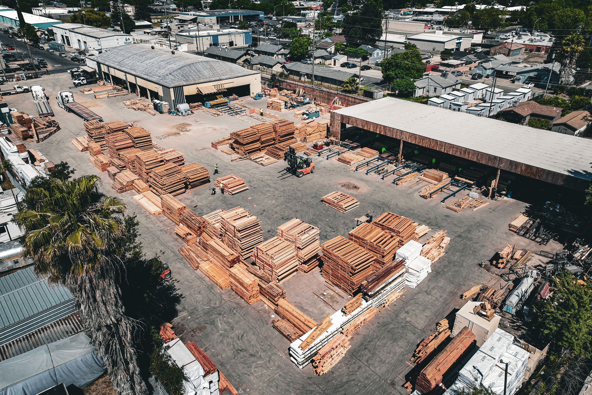Aerial view of a lumber yard with stacks of cut wood and industrial buildings.