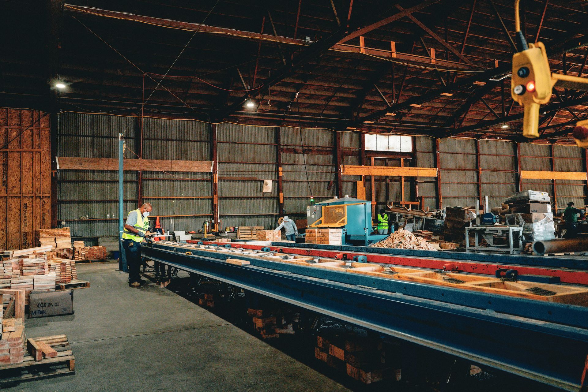 Worker in a large warehouse beside a long blue conveyor line and stacks of materials