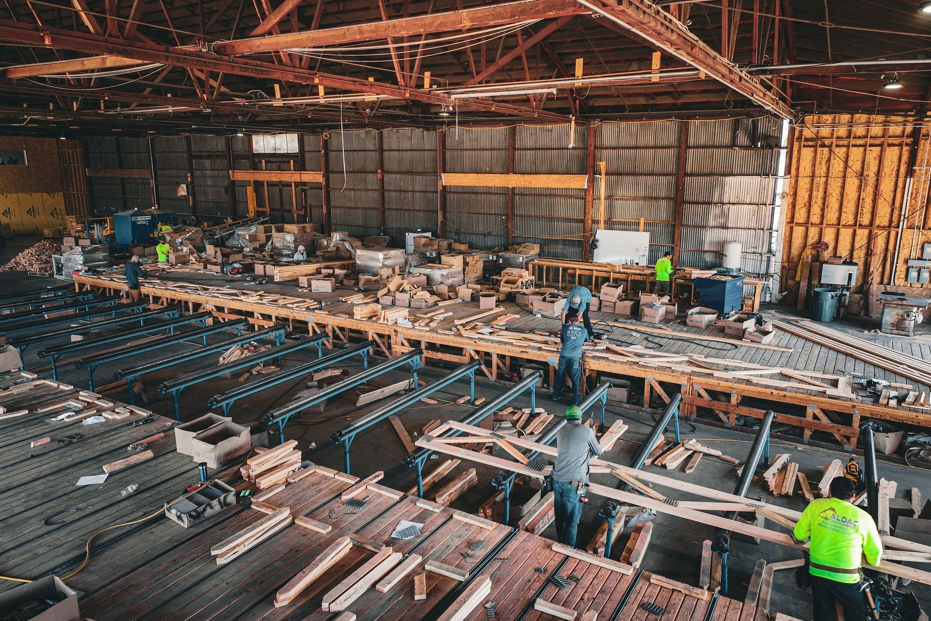 Workers in a large industrial warehouse sorting materials and machinery parts under a high metal roof