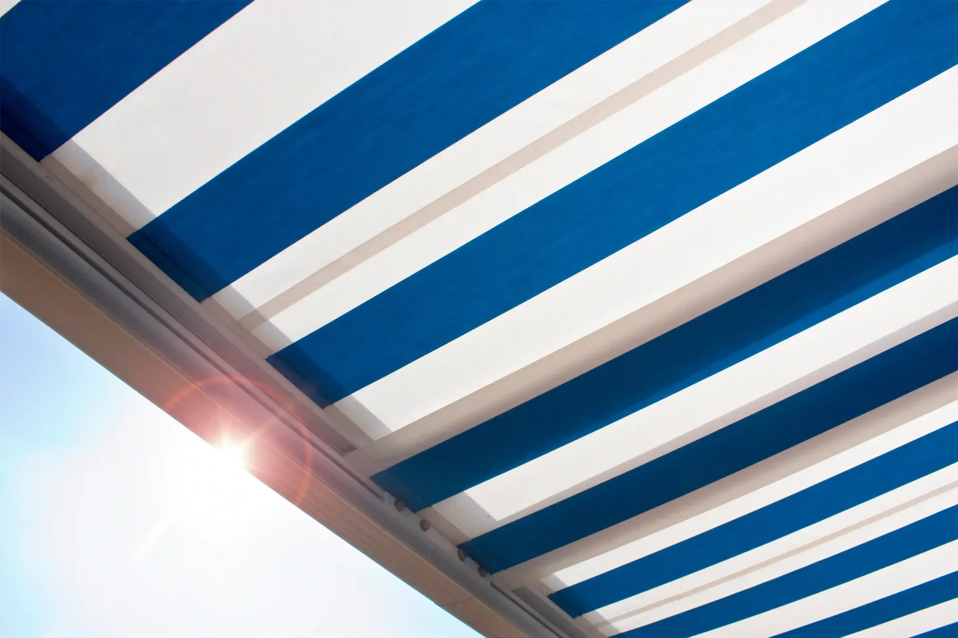 Blue and white striped manual retractable awning extended on a high-rise balcony under bright sunlig