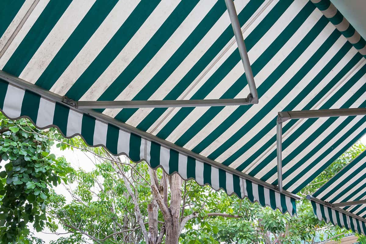 Close-up of a green and white striped fabric canopy with retractable arms, a standard feature affect
