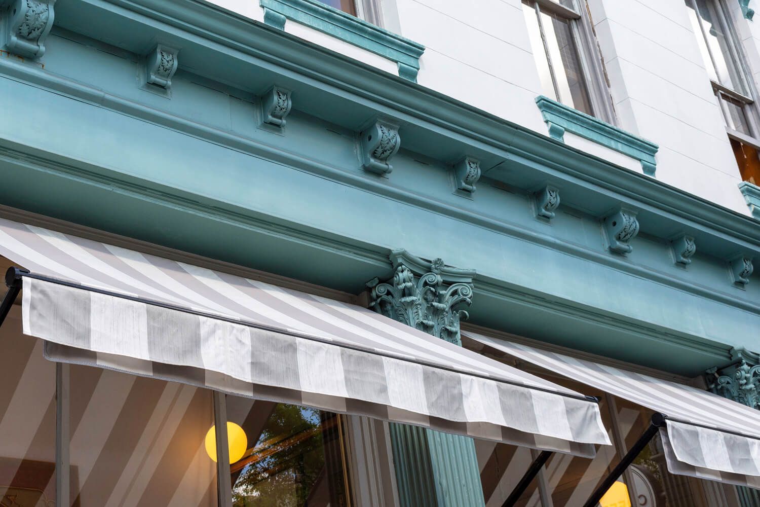 Sun-faded striped awning cover on a commercial building facade in need of awning fabric replacement.