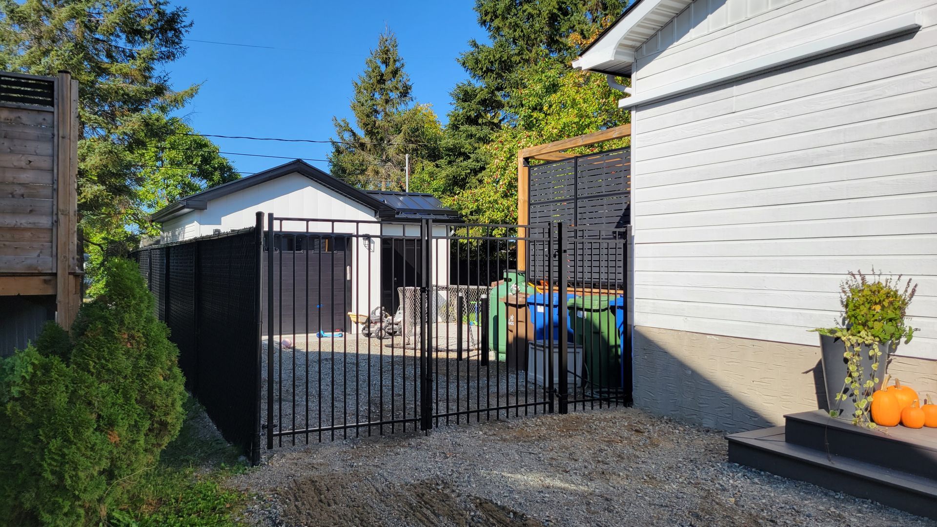 Une clôture en métal noir entoure une cour latérale avec un garage et une maison par une journée ensoleillée.