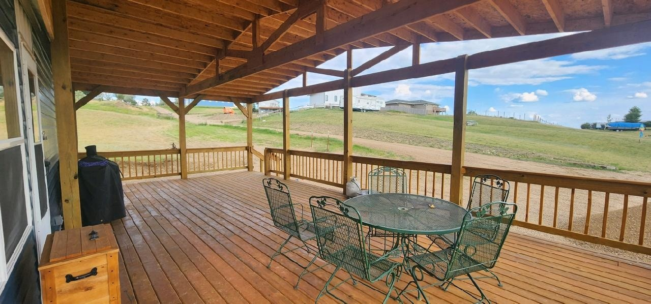 A spacious, wooden covered deck overlooking a grassy hillside with outdoor metal furniture and a grill.