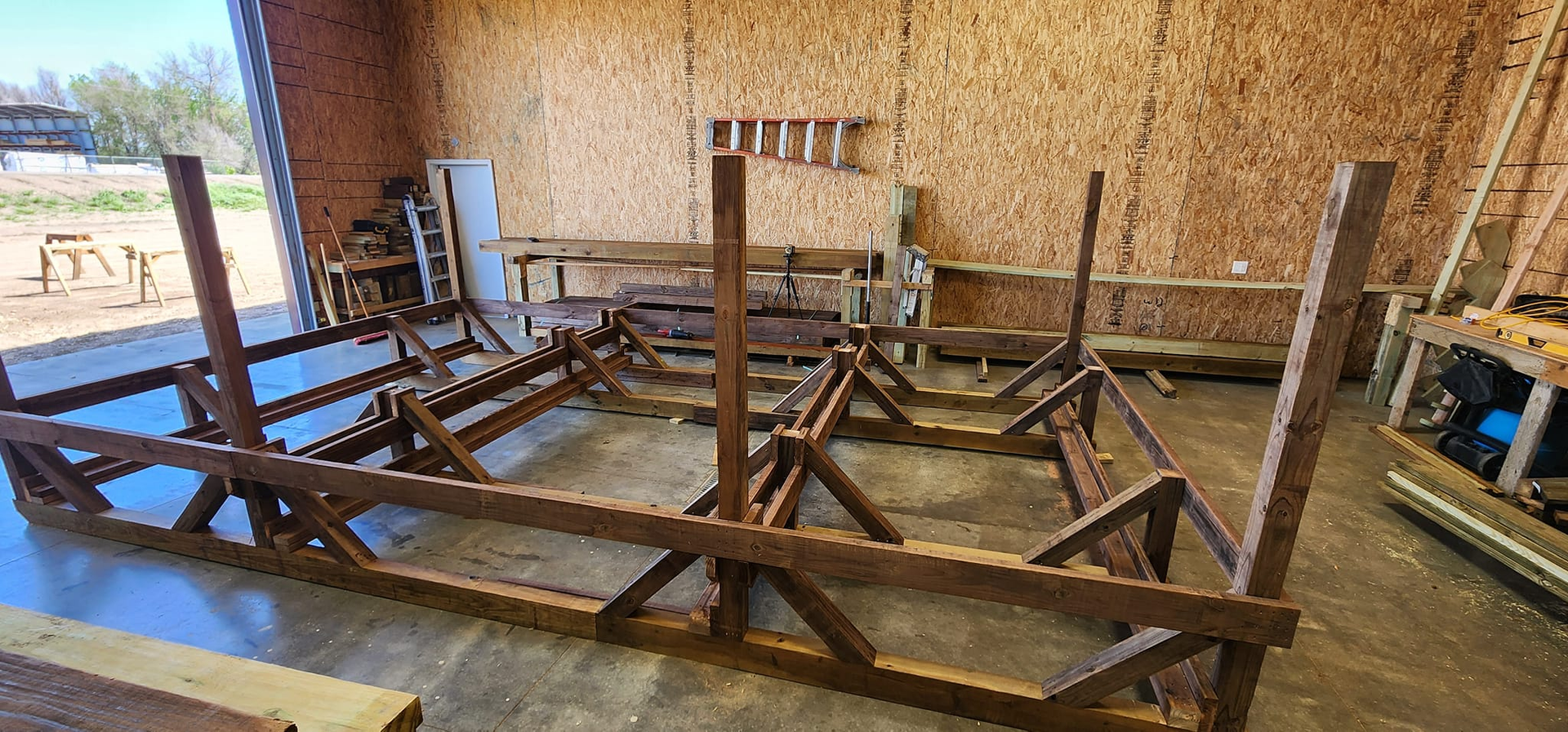 A wooden construction frame consisting of vertical posts and horizontal support beams inside a large workshop.