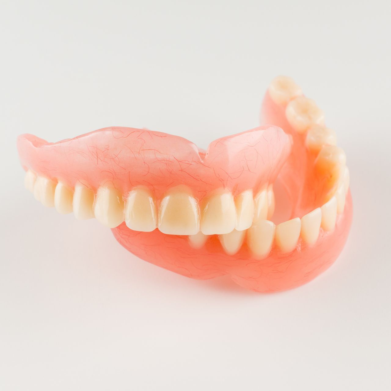 Full set of dentures, pink base with white artificial teeth, against a white background.