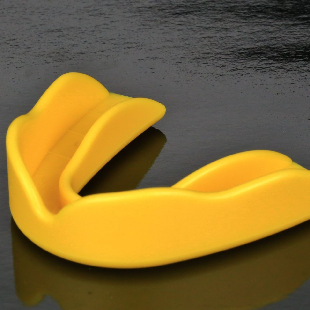 Yellow mouthguard on a reflective black surface, for athletic protection.