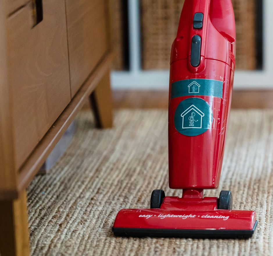Red handheld vacuum cleaner on a textured rug near a wooden cabinet.