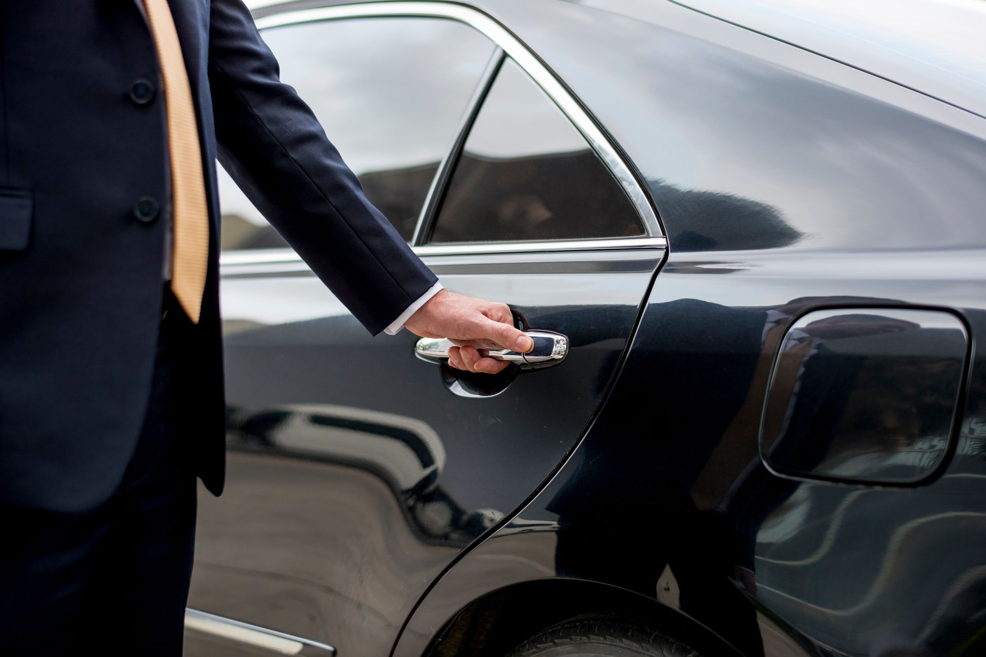 Person in a dark suit opening the door of a black car