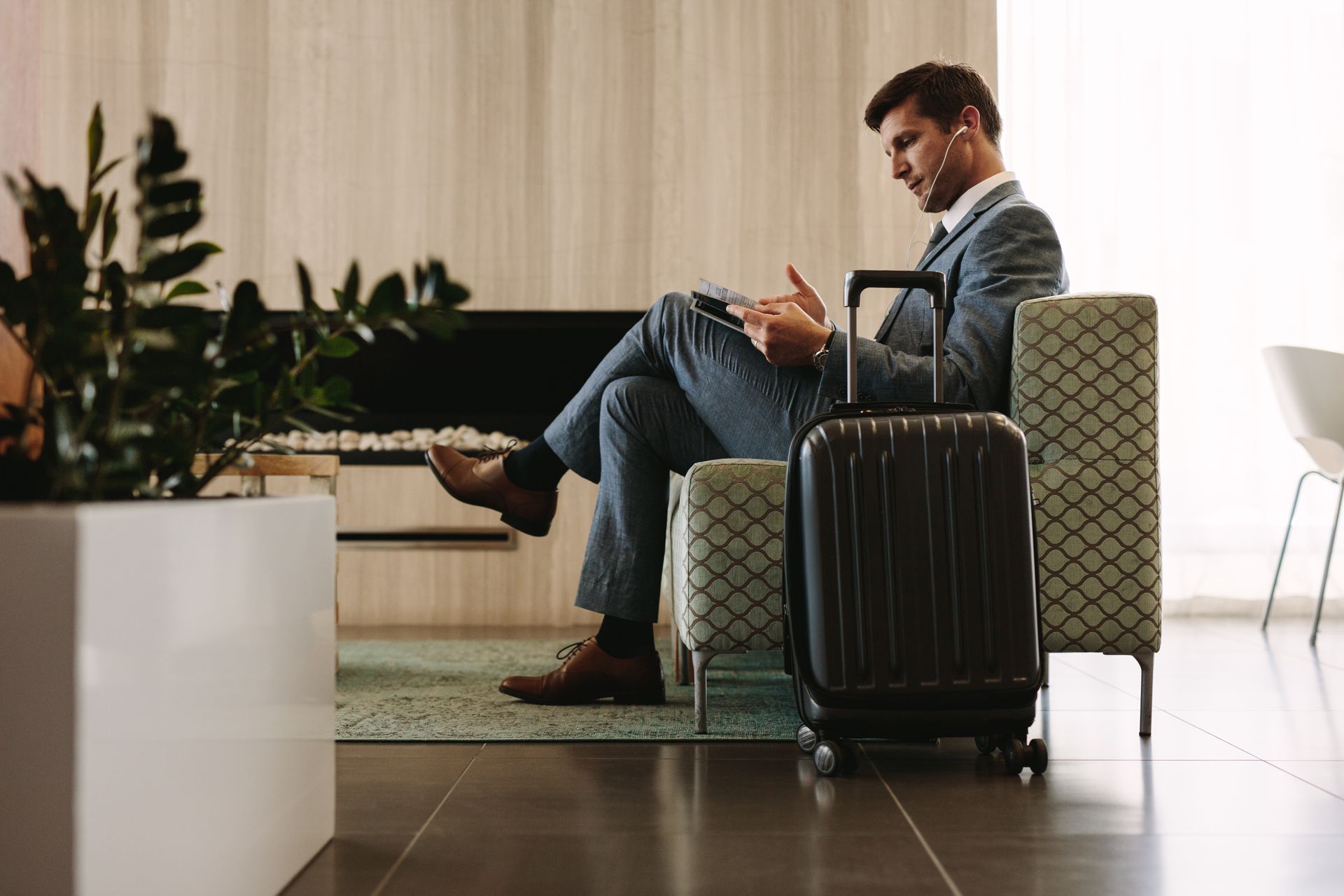 Man sitting with a tablet beside a black suitcase in a modern hotel lobby